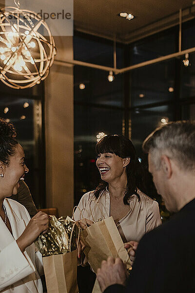 Männliche und weibliche Kollegen lachen  während sie Geschenktüten in der Firma während einer Party halten