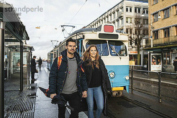 Paar hält Hände beim Gehen an der Straßenbahnhaltestelle