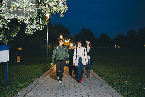 Glückliche männliche und weibliche Freunde zu Fuß in Campus in der Nacht