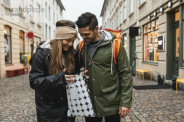 Lächelnde Paar späht in Einkaufstasche  während auf der Straße stehen