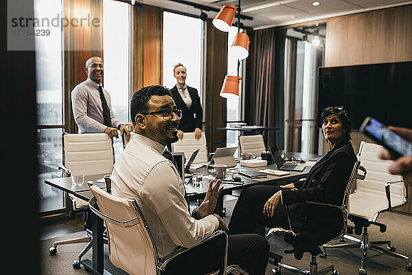 Multi-ethnische Kollegen  die einen älteren Geschäftsmann während einer Besprechung im Vorstandszimmer ansehen
