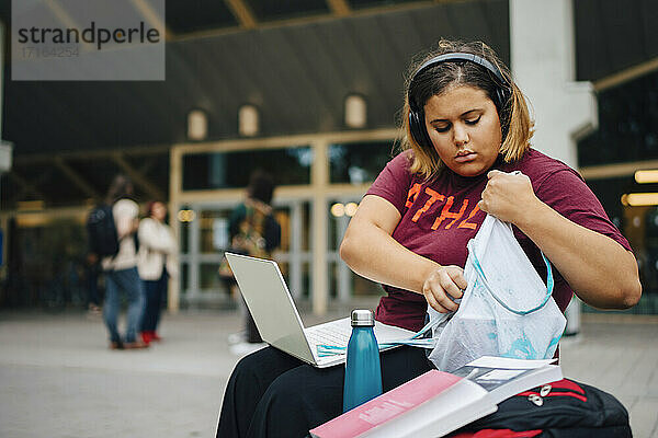 Weibliche Studentin späht in Tasche beim Sitzen in der Universität