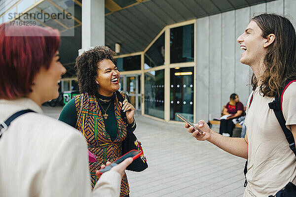 Junge Universitätsstudenten lachen  während sie sich auf dem College-Campus miteinander unterhalten
