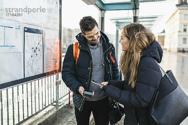 Lächelnde Frau scannt QR-Code durch Smartphone steht neben Mann am Bahnhof