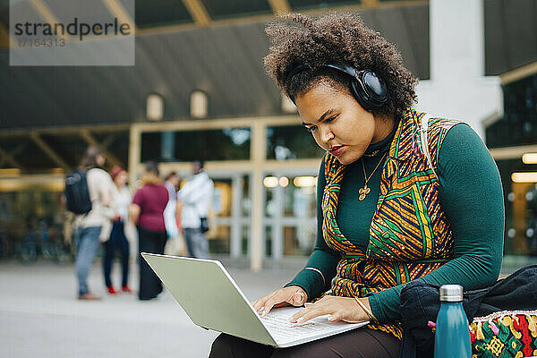 Weibliche Studentin konzentriert sich beim Online-Lernen über einen Laptop auf dem College-Campus