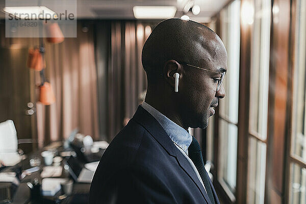 Profilansicht eines glatzköpfigen Geschäftsmannes mit In-Ear-Kopfhörern im Sitzungssaal eines Büros