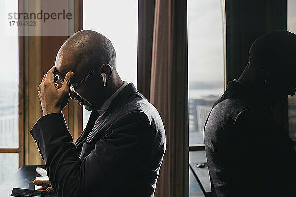 Besorgter männlicher Unternehmer mit In-Ear-Kopfhörern  der im Sitzungssaal auf sein Smartphone schaut