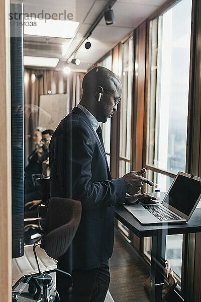 Seitenansicht des glatzköpfigen männlichen Unternehmers mit Laptop im Sitzungssaal durch eine Glaswand gesehen