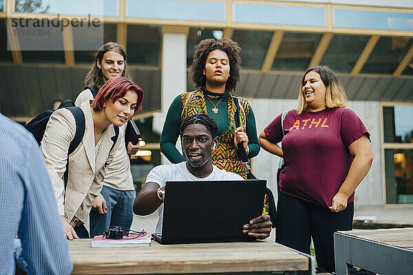 Glückliche männliche und weibliche Freunde studieren online durch Laptop in Universitätscampus