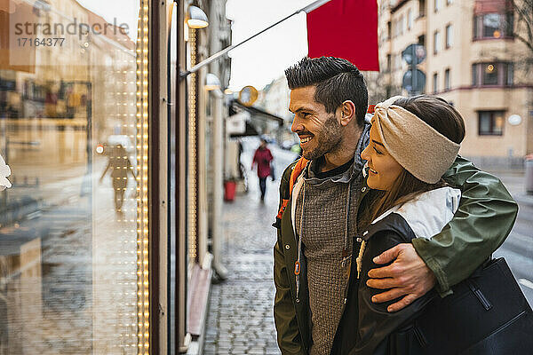 Lächelnder Mann Arm um Frau beim Schaufensterbummel in der Stadt