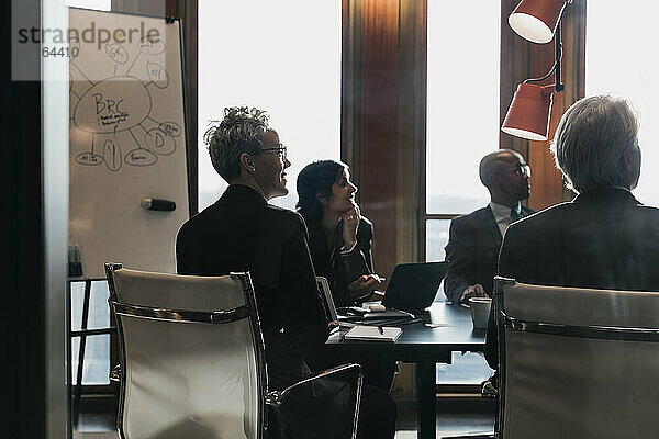Geschäftskollegen  die wegschauen  während sie am Konferenztisch sitzen und eine Strategie im Vorstandszimmer planen  während einer Sitzung im Off
