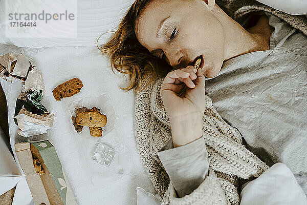 Hohe Winkel Ansicht der Frau essen Keks  während auf dem Bett zu Hause liegen