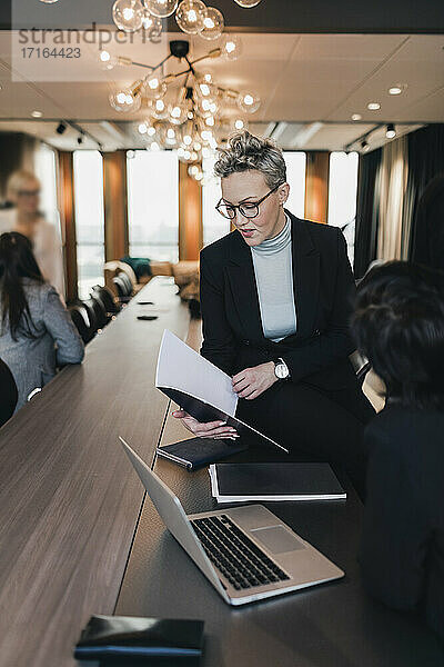 Reife Geschäftsfrau diskutiert über Dokument mit weiblichen Kollegen am Konferenztisch im Sitzungssaal