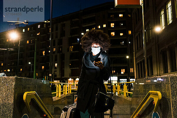 Frau mit Gesichtsmaske  die auf ihr Telefon schaut  auf Reisen in der Nacht