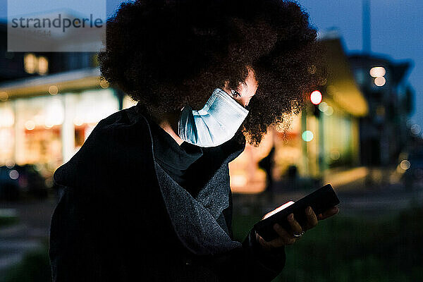 Frau mit Gesichtsmaske  Blick auf das Telefon  nachts im Freien