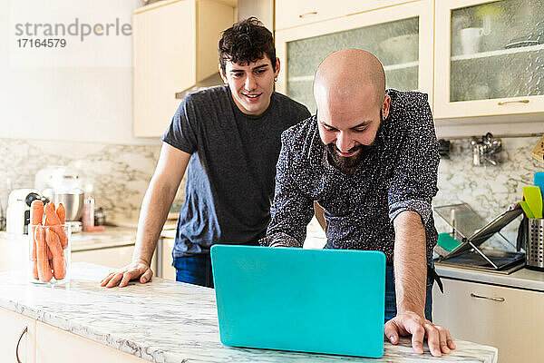 Junge Männer schauen auf einen Laptop in der Küche