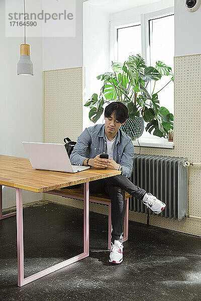 Junger Mann mit Telefon und Laptop im Co-Working Space