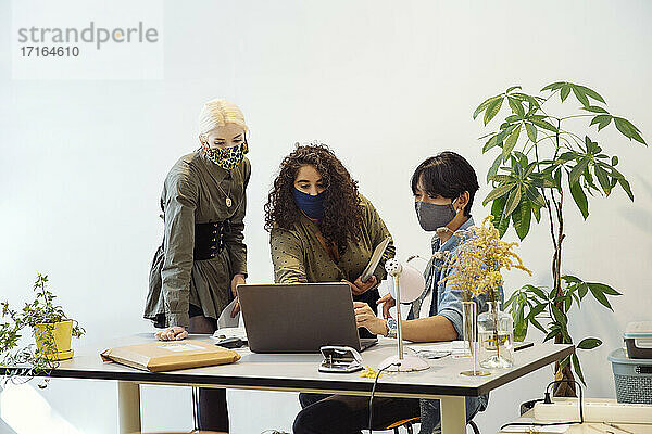 Kollegen mit Gesichtsmasken  die auf einen Laptop schauen
