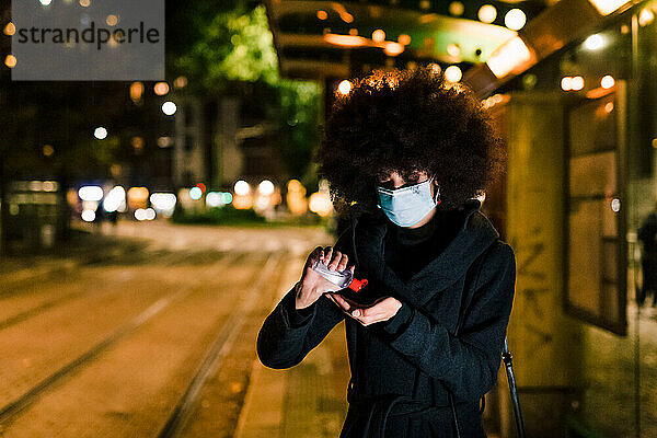 Frau benutzt Handdesinfektionsmittel  trägt Gesichtsmaske  nachts im Freien
