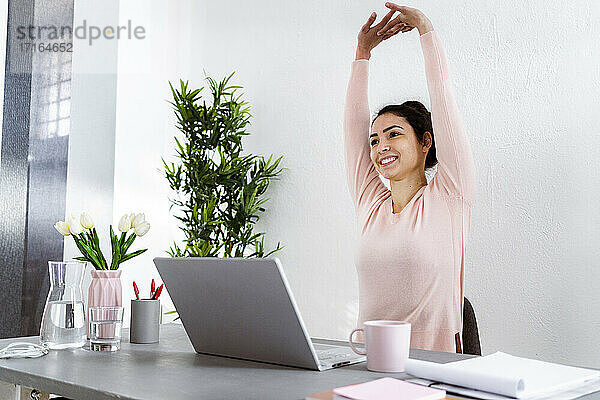 Young woman with hand raised using laptop while sitting at home office