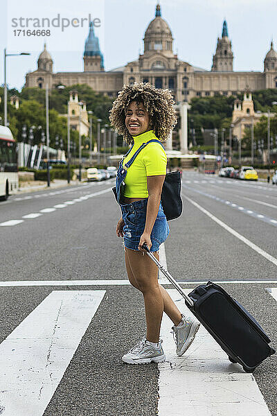 Lächelnde Frau mit Gepäck auf der Straße in der Stadt spazierend