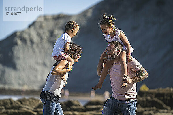 Cheerful parents carrying children on shoulder at beach
