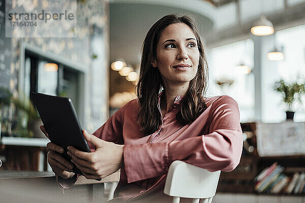 Weibliche Fachkraft mit digitalem Tablet  die wegschaut  während sie in einem Café sitzt