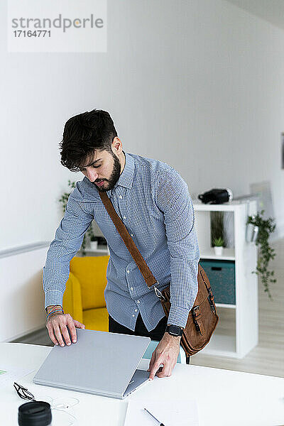 Junger Geschäftsmann schließt Laptop am Schreibtisch in einem kreativen Büro
