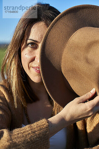 Woman holding hat in front of face