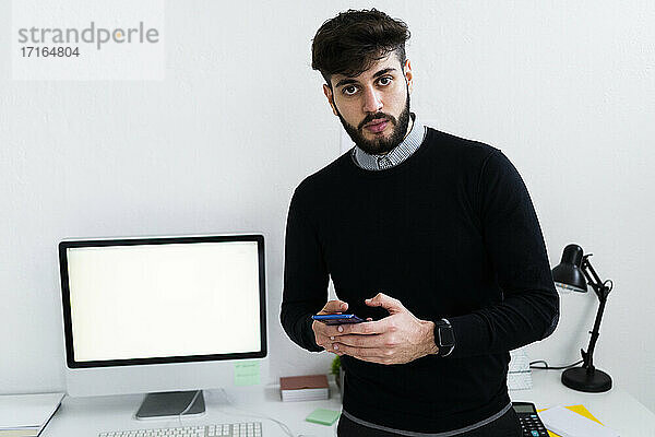 Porträt eines Geschäftsmannes  der ein Smartphone im Büro hält