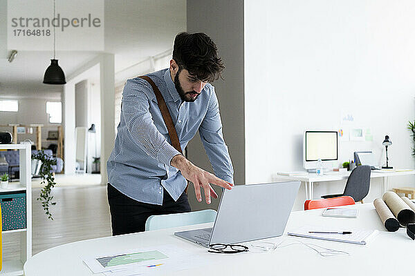 Junger Geschäftsmann schließt Laptop am Schreibtisch in einem kreativen Büro