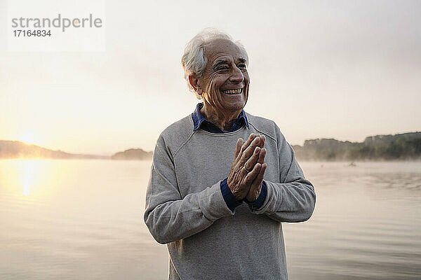 Lächelnder Mann  der mit verschränkten Händen am See steht