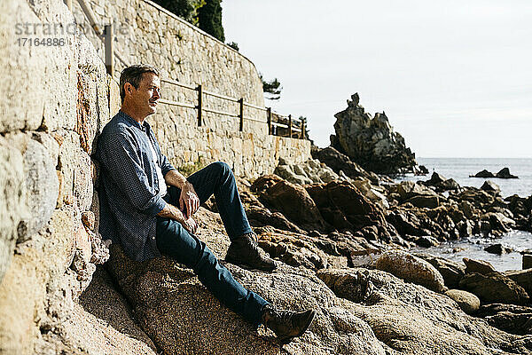 Nachdenklicher Mann auf einem Felsen am Strand sitzend an einem sonnigen Tag