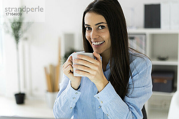 Lächelnde Geschäftsfrau  die im Büro sitzend Kaffee trinkt