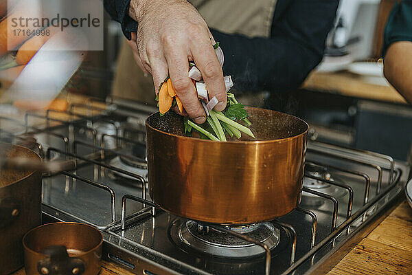 Chef putting vegetables in copper saucepan while making Broth soup in kitchen