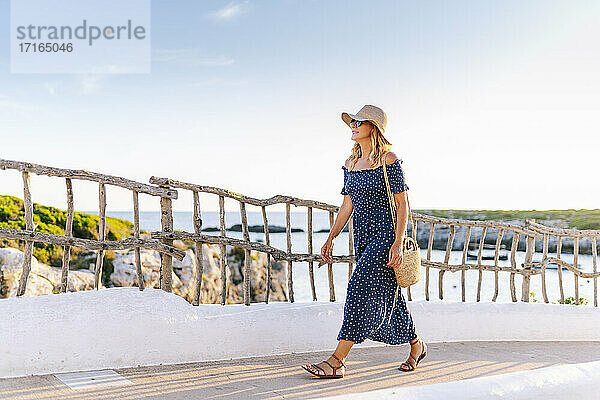 Weibliche Touristin mit Hut auf dem Fußweg gegen den Himmel im Dorf Binibeca  Menorca  Spanien
