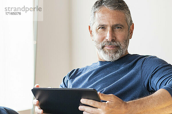 Selbstbewusster Geschäftsmann  der ein digitales Tablet benutzt  während er zu Hause sitzt