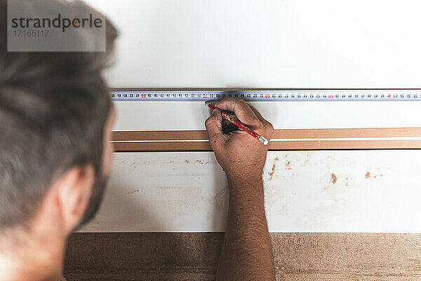 Young male carpenter marking on wood using tape measure while working in workshop