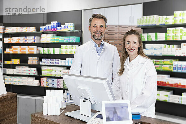 Smiling male and female pharmacist standing at checkout in store