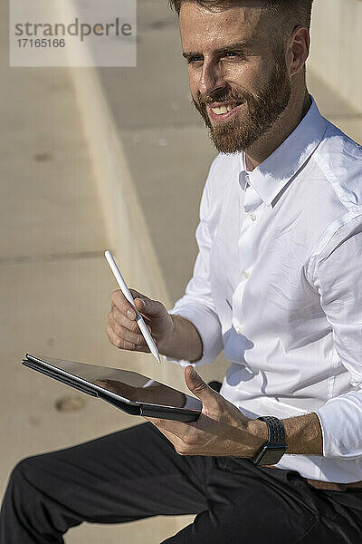 Businessman smiling while using digital tablet sitting on steps