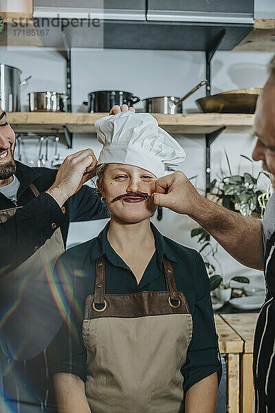 Playful chefs having fun with colleague while standing in kitchen