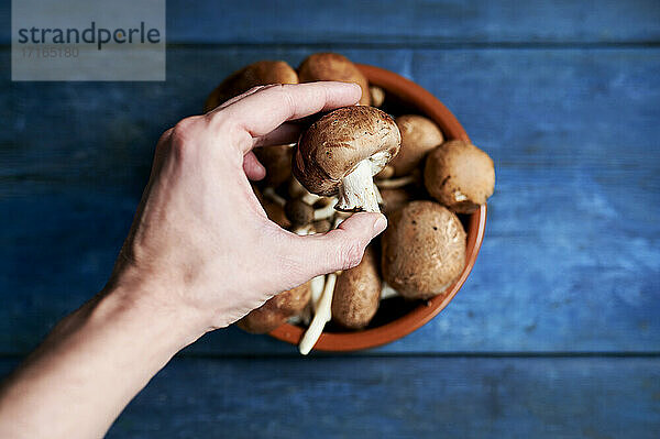 Hand of man picking up brown mushroom from bowl