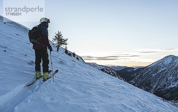 Male skier at snowcapped summit during sunrise
