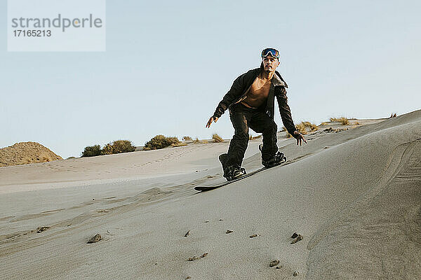 Junger Mann schaut beim Sandboarding gegen den klaren Himmel in Almeria  Tabernas-Wüste  Spanien  weg
