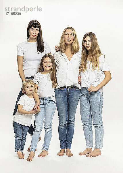 Confident mothers and daughters standing against white background in studio