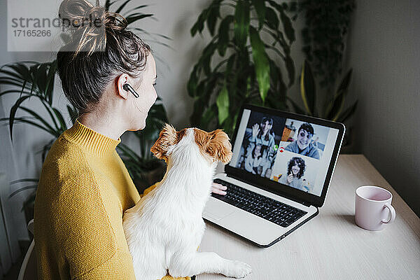 Woman talking with friends on video conference over digital tablet while sitting with pet at home