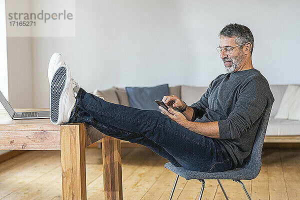 Lächelnder Geschäftsmann  der ein Mobiltelefon benutzt  während er zu Hause im Büro sitzt