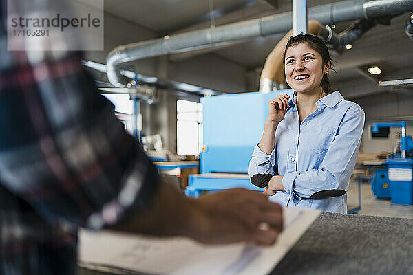 Smiling businesswoman working with colleague while standing at industry