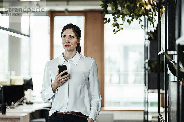 Geschäftsfrau mit Mobiltelefon im Büro stehend