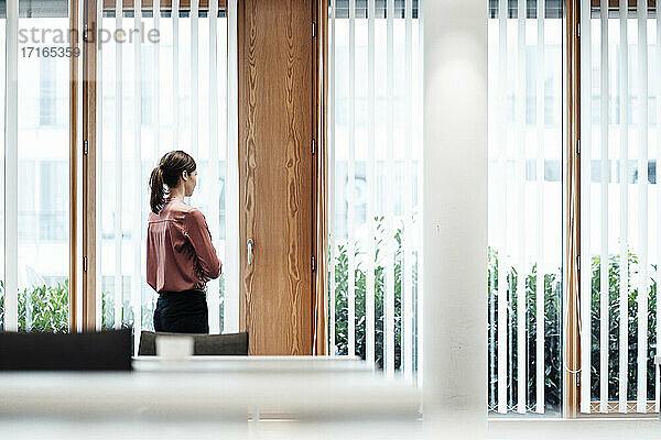 Geschäftsfrau schaut durch ein Fenster  während sie im Büro steht